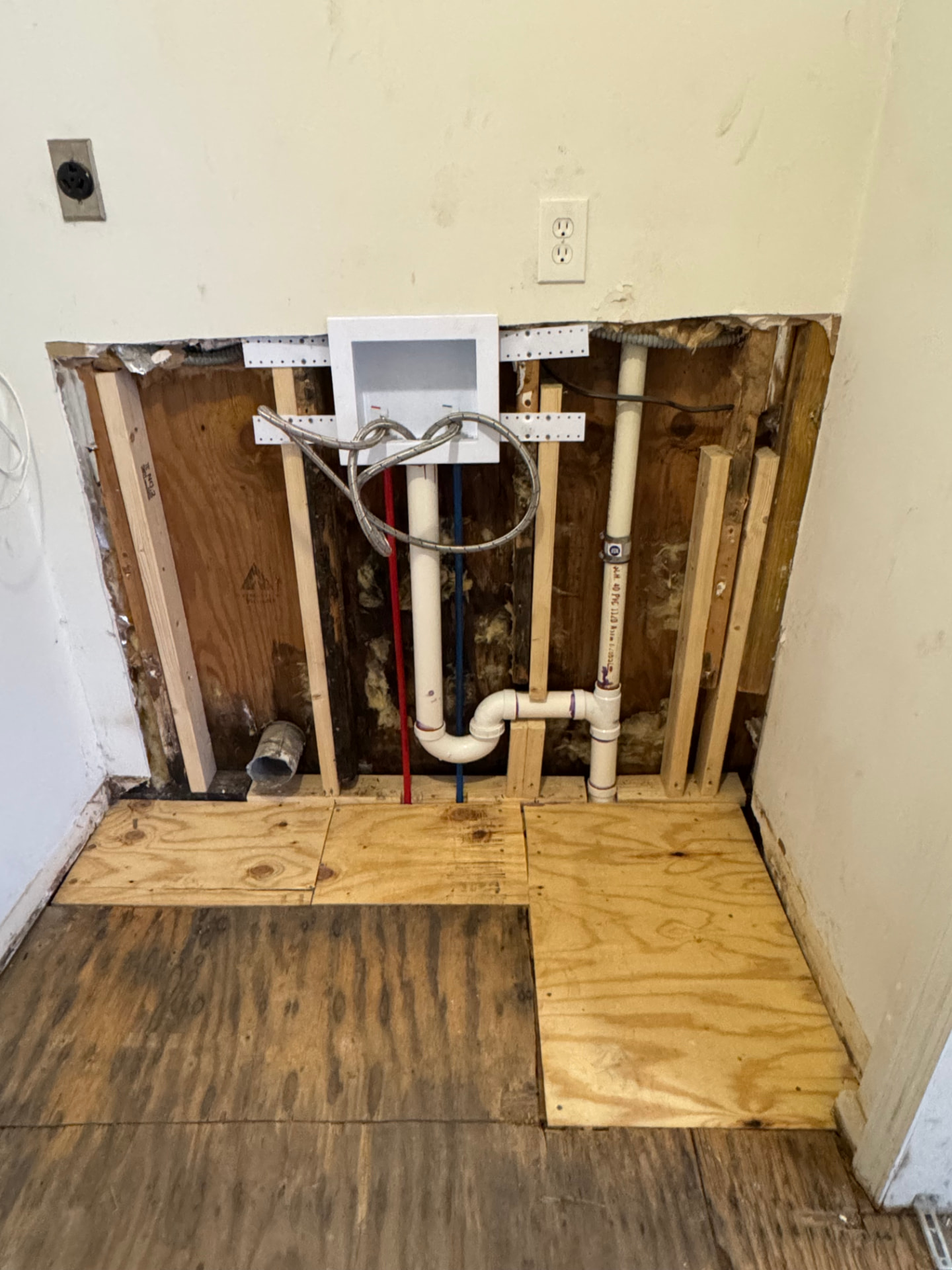 Open wall showing new laundry box, water lines, drain, and framing repair